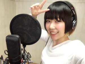 おかっぱミユキの歌のレコーディング風景写真。コンデンサーマイクを前に笑顔でピースサインしている。