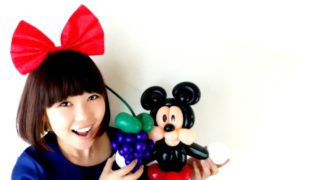 つくったバルーンアートを見せているおかっぱミユキの写真。ミッキーマウスと葡萄のバルーンアートを持って、ニコニコしている。