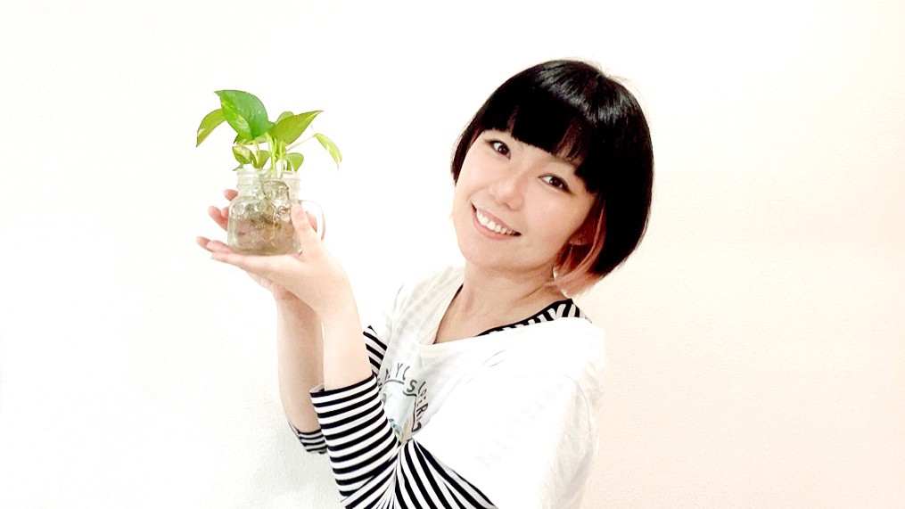 観葉植物を持っているおかっぱミユキの写真。水栽培のポトスを持って笑顔で嬉しそうにしている。