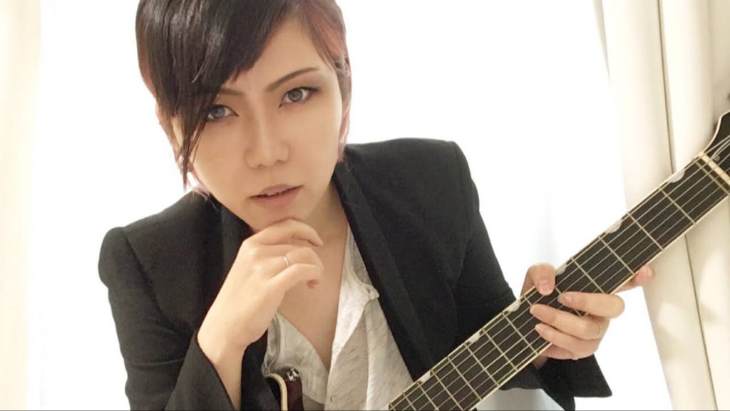 ビジュアル系ギタリストに扮するおかっぱミユキの写真。男装してギターを担ぎ、格好つけている。