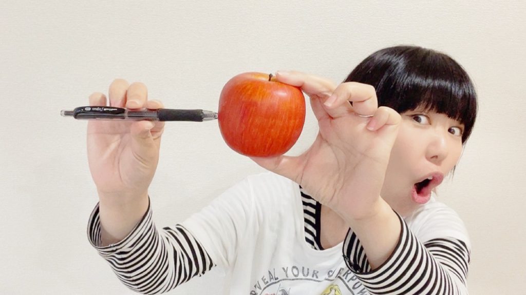 楽しそうな表情で、りんごにペンを刺しているおかっぱミユキの写真