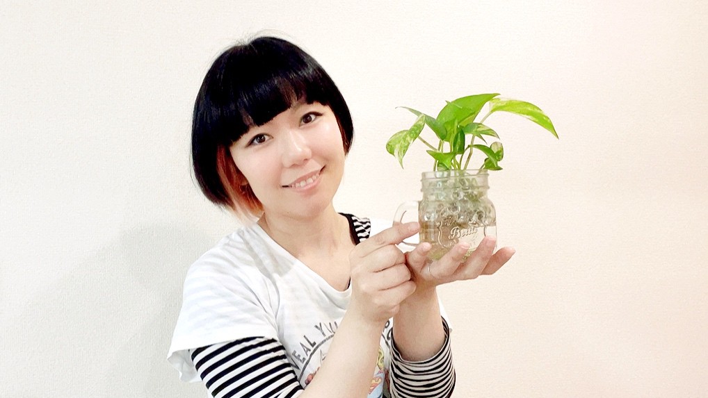 観葉植物を持っているおかっぱミユキの写真。水栽培のポトスを持って笑顔で嬉しそうにしている。