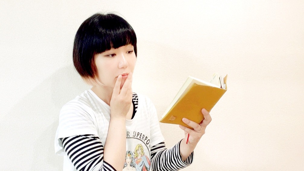 読書をしているおかっぱミユキ。革製のブックカバーがついている文庫本を書か手で持ち、面白そうな表情をしている。