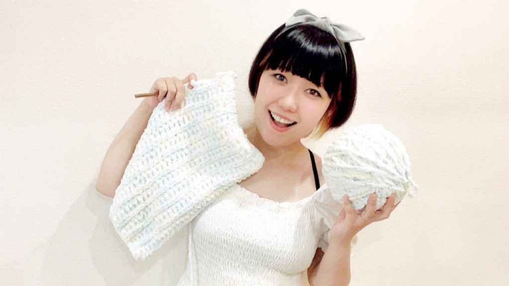 編み物をしているおかっぱミユキの写真。右手に編みかけのニットを、毛糸の玉を持って、楽しそうに笑っている。