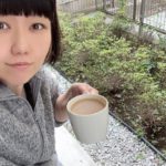 庭でカフェオレを飲んでいるおかっぱミユキの写真。肌寒いのか、モコモコのアウターを着ている。