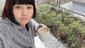 庭でカフェオレを飲んでいるおかっぱミユキの写真。肌寒いのか、モコモコのアウターを着ている。