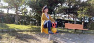 公園で遊具に座るおかっぱミユキ。エビフライのような形の遊具に座って、空を眺めている。