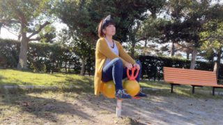 公園で遊具に座るおかっぱミユキ。エビフライのような形の遊具に座って、空を眺めている。