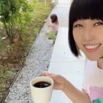 コーヒーカップを片手に微笑むおかっぱミユキの写真。自宅の庭で子供が遊んでいる。